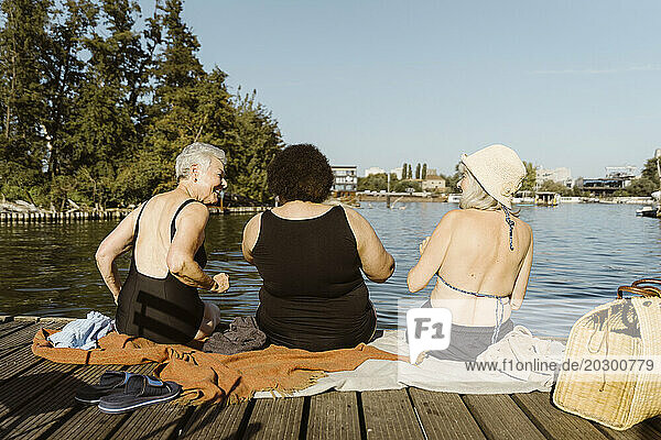 Rear view of female senior friends having fun while sitting on houseboat near lake