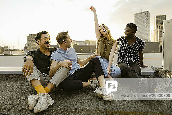 Happy woman raising hand while sitting with male friends on terrace