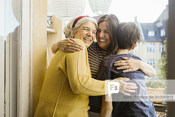 Happy woman embracing mother-in-law and son while standing in balcony
