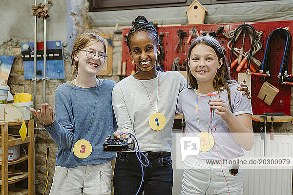 Portrait of happy female students showing electrical parts during technology workshop at school