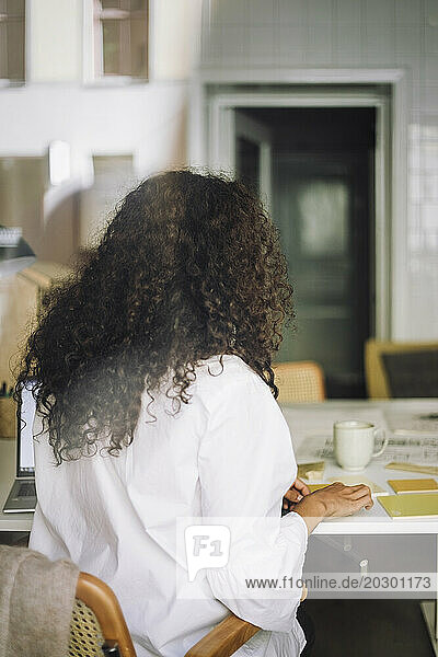 Rear view of female architect with curly hair working while sitting at office