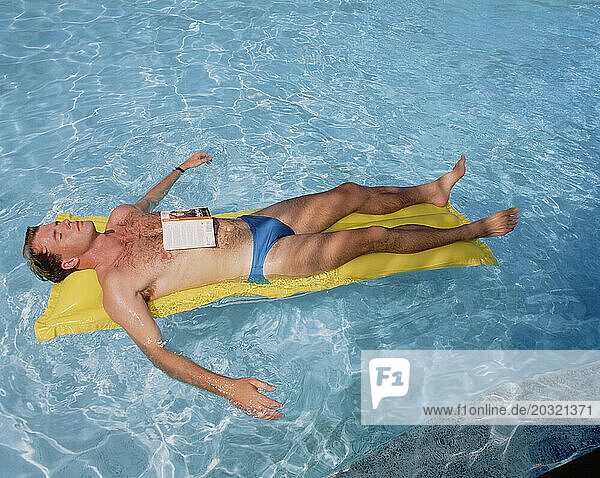 Young man reclining on airbed in swimming pool.