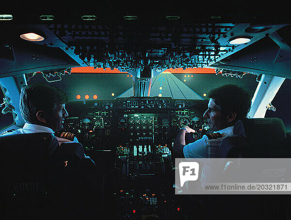 Two pilots at aircraft controls. Boeing 747 jumbo jet flight deck. Simulated runway at sunset.