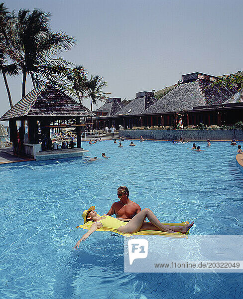 Australia. Queensland. Lindeman Island resort. Young man & woman relaxing on lilo in swimming pool.