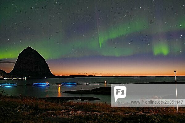 Nordlichter (aurora borealis) vermischen sich mit Sonnenuntergang  Meer  markante Berge und Fischfarm  Lovunden  Helgelandsküste  Traena  Norwegen  Europa