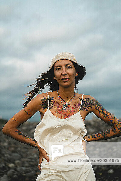 Young happy tattooed woman in a dress on a windy rocky beach.