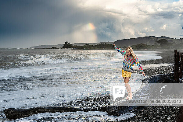 Girl walking on log at beach with rainbow