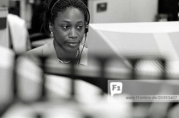 An African American woman works in an office building as a receptionist wearing a headphone to receive and make calls.