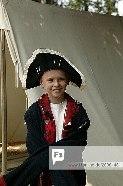 A young caucasian boy dresses in Civil War clothing at a historical site in the south.