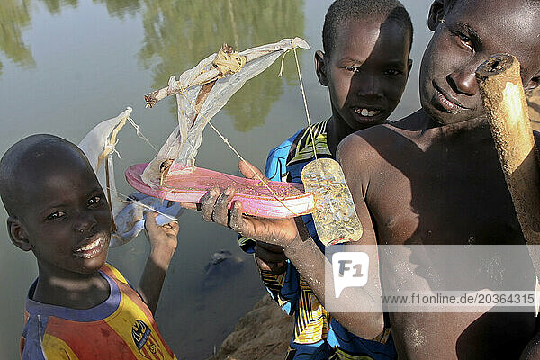 Three Songhai children show off a toy boat made from a sandal and sardine can lid by the Niger River  Mali  West Africa
