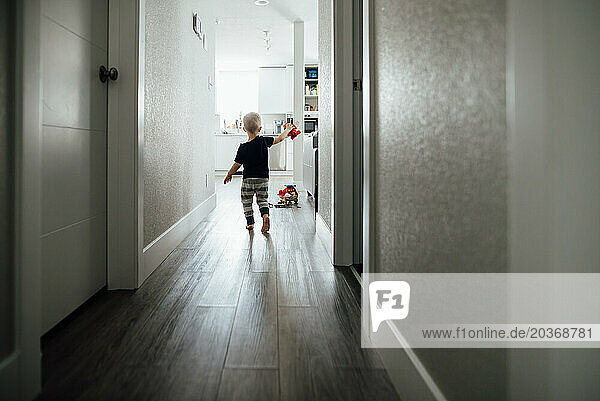 Rear view of small boy walking down hallway pretending to fly plane