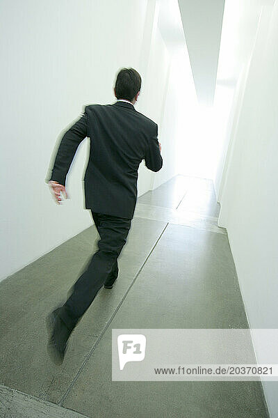 A man running down a long hallway toward a bright light.