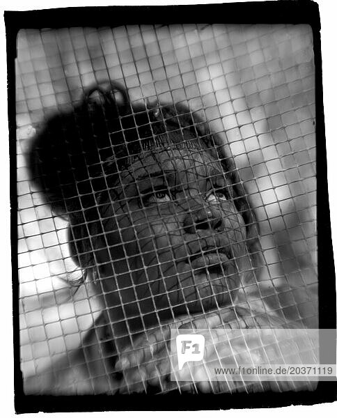 A young African American girl prays as she looks towards the sky through a fence. (Polaroid)