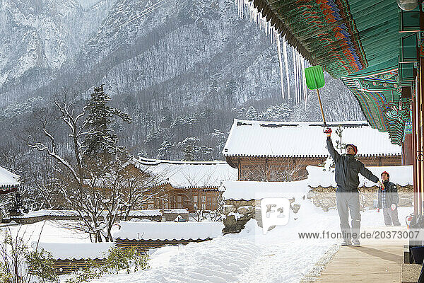 Monk removing ice from roof of Buddhist Sinheung-sa temple in Seoraksan National Park  Gangwon-do  South Korea