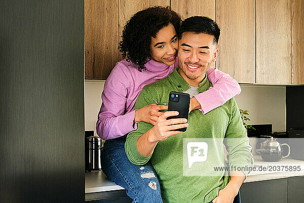 Multiethnic happy couple using the smartphone together in the kitchen.
