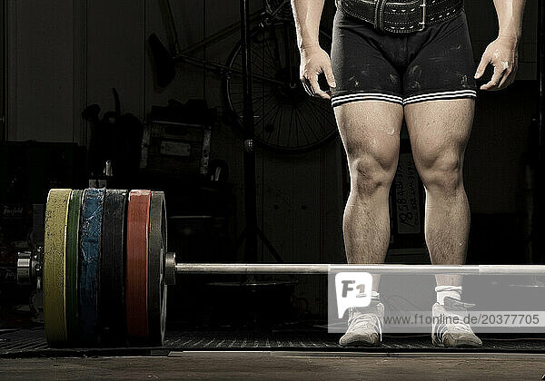 The legs of a Korean male power lifter standing with weights.