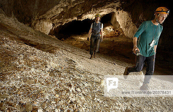 Two cave explorers walk through a section of cave tunnel deep in heart of the mountain. At this point in the cave the floor was