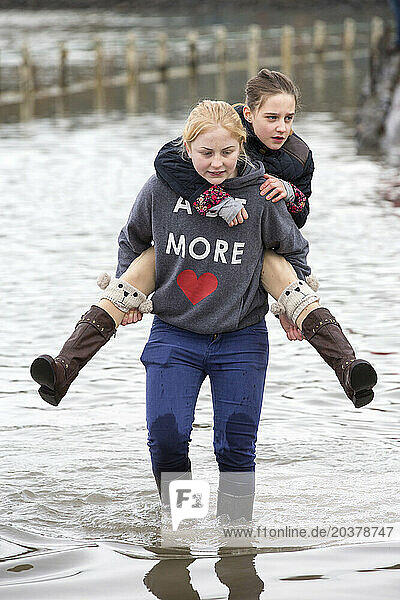 Teenage girls wading in flooded street in Storth at Kent river estuary