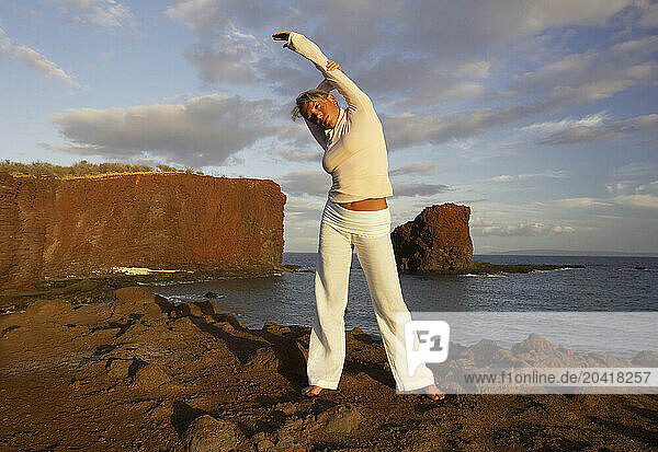 Young woman stretching by the Pacific Ocean before exercise on rocks in Lanai Hawaii