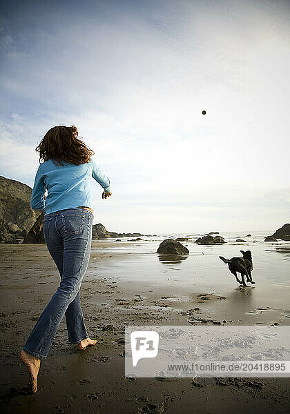 A woman throws a ball for her dog as the sun sets on Muir Beach in northern California