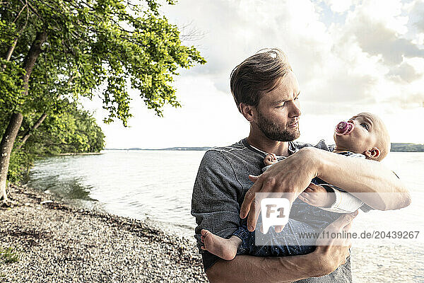 Father holding baby girl in arms at lake