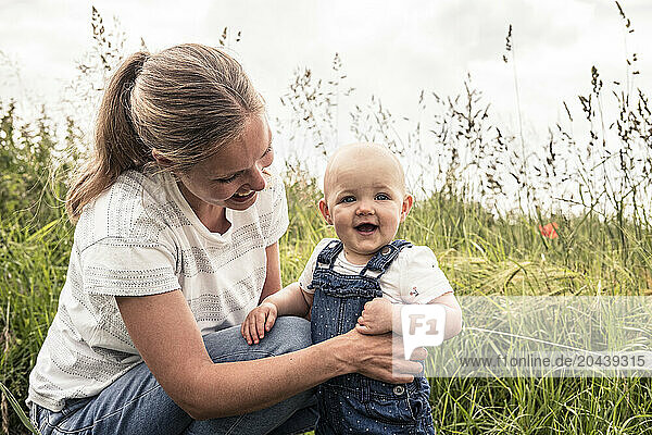 Smiling mother holding daughter in meadow
