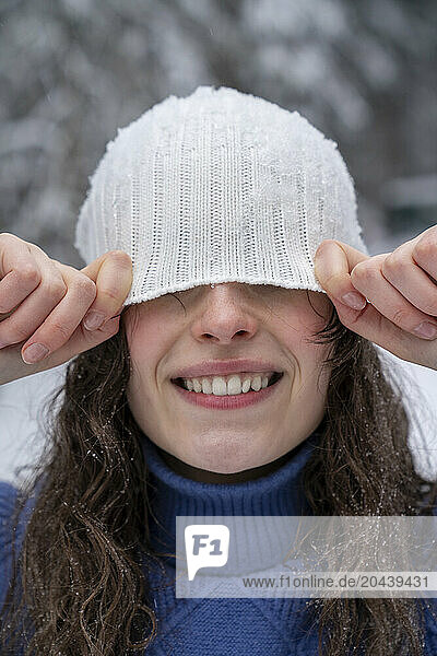 Young woman hiding face with knit hat in winter forest