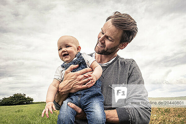 Father holding daughter in arms and standing in meadow