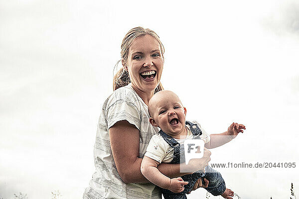 Cheerful mother holding daughter in arms under clear sky