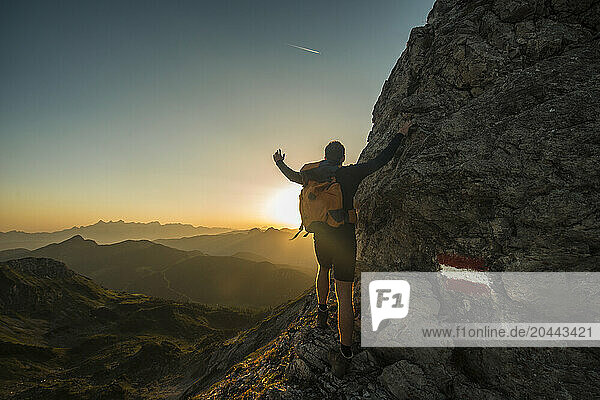 Carefree young man standing on Steinfeldspitze rock under sky at sunrise in Altenmarkt  Zauchensee  Salzburg  Austria