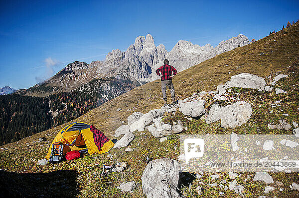 Senior man standing with hands on hip near tent and looking at mountain