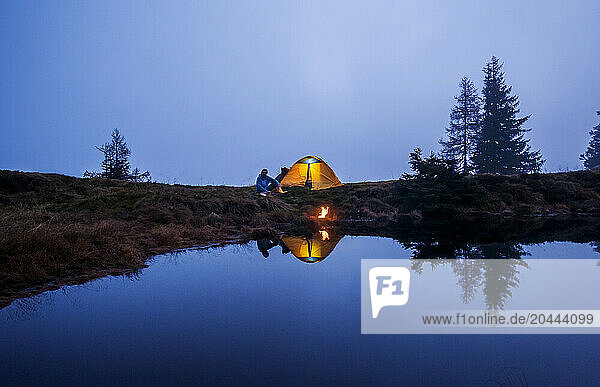 Senior man camping near lake at dusk
