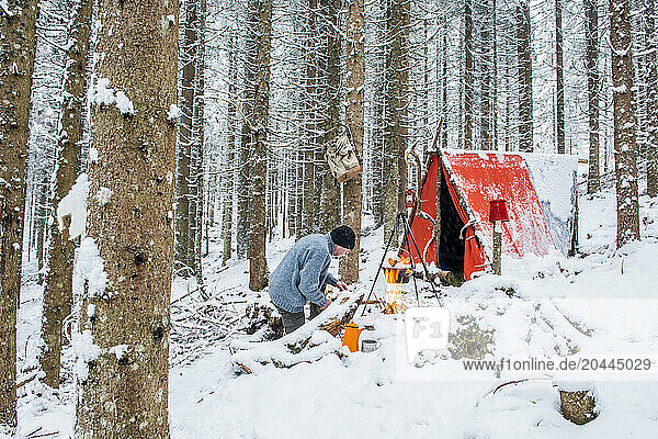 Senior man preparing campfire in snow near tent