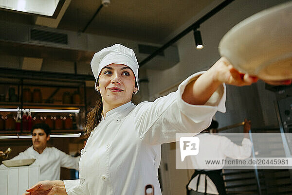 Low angle view of smiling female chef passing bowl while working in commercial kitchen