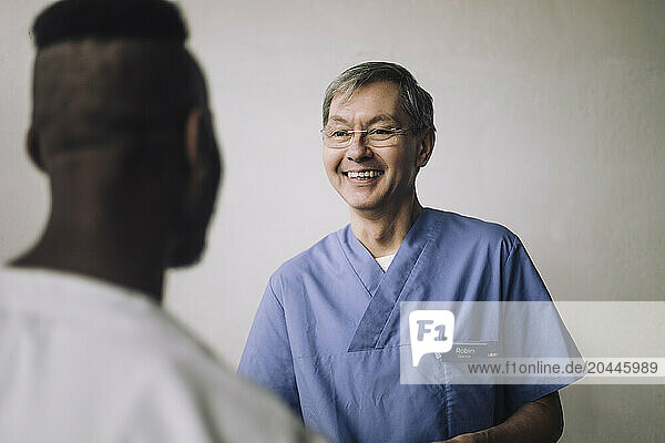 Smiling senior male medical professional talking with colleague near wall