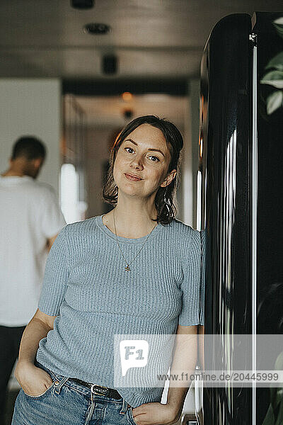 Portrait of beautiful woman leaning on refrigerator with hands in pockets at home