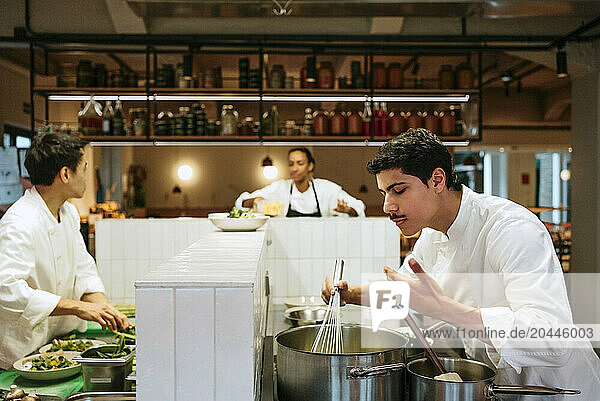 Male chef smelling food aroma while cooking with colleagues in commercial kitchen