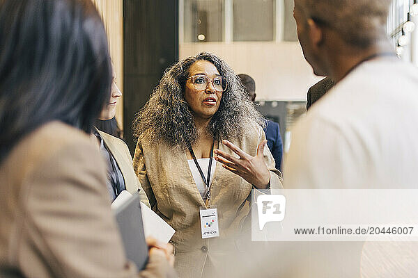 Mature female entrepreneur discussing with delegates during networking event at convention center