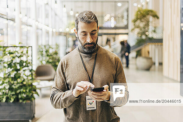 Mature businessman using phone while standing at convention center