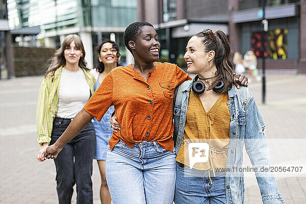 Happy women walking with arms around in city