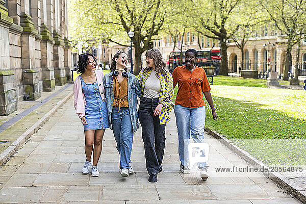 Happy multiracial female friends walking together on footpath