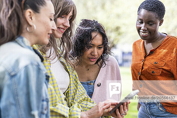 Young woman sharing smart phone with friends at park