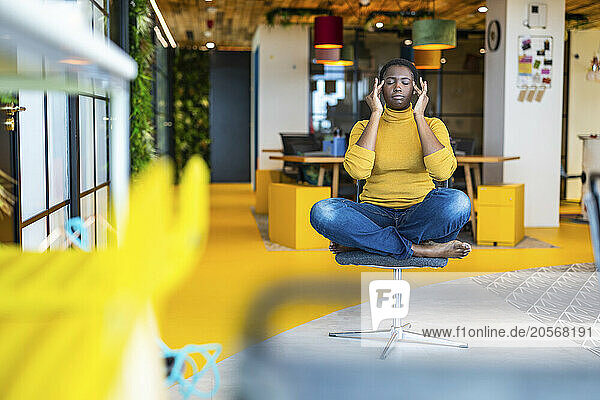 Businesswoman touching temples sitting on chair at office