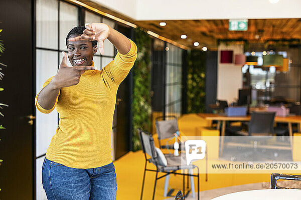 Smiling businesswoman making finger frame at office