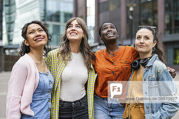 Smiling female friends looking up standing in city