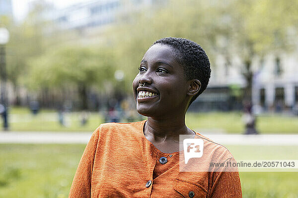 Smiling woman with short hair wearing orange top looking away at park