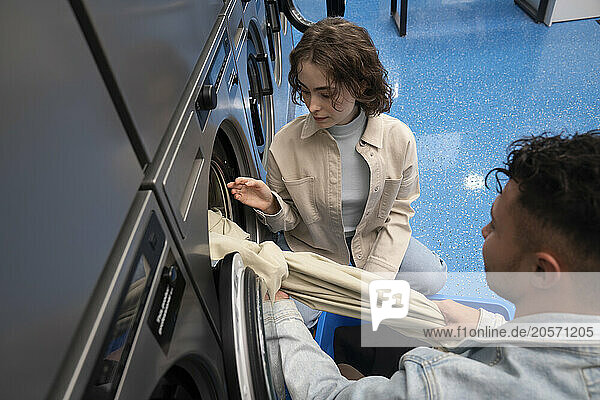 Young woman and man removing sheet from washing machine in laundromat
