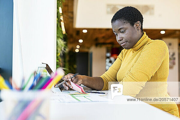 Focused businesswoman reading adhesive note and sitting with laptop at coworking space