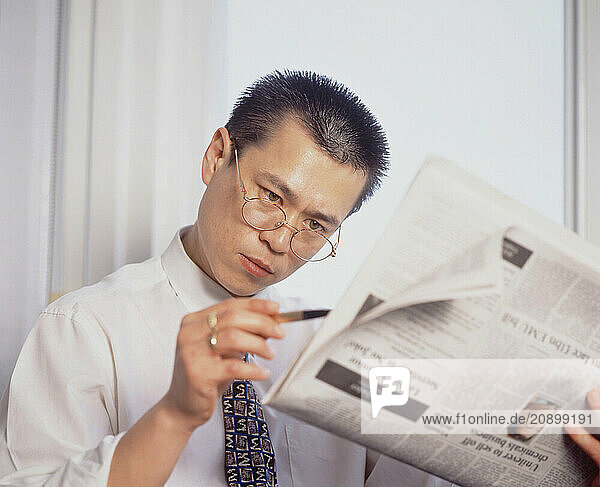 Business & Professions. Young man in office  sitting reading newspaper.