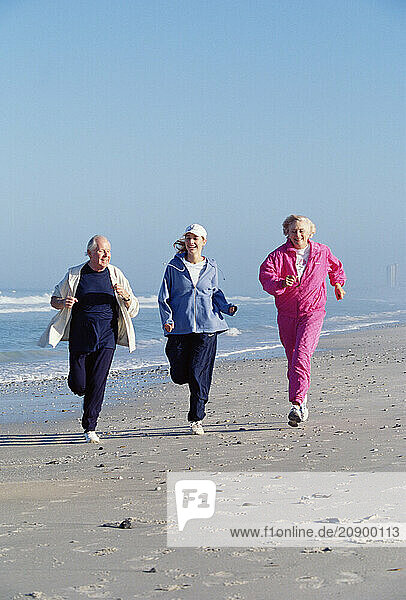 Senior man & woman with young woman running on a beach.